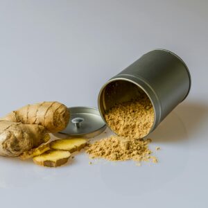 Close-up of fresh ginger root with sliced pieces and ginger powder spilled from a metal container.