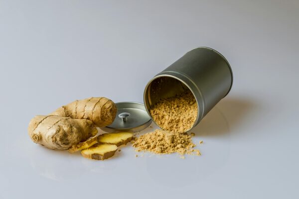 Close-up of fresh ginger root with sliced pieces and ginger powder spilled from a metal container.