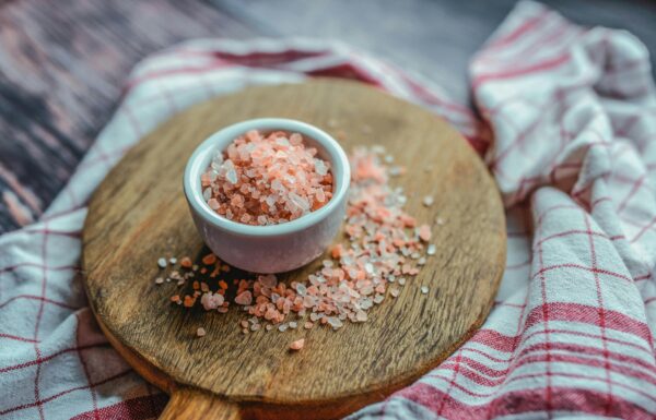 A close-up shot of pink Himalayan salt in a ceramic cup on a wooden board. Ideal for culinary and health visuals.