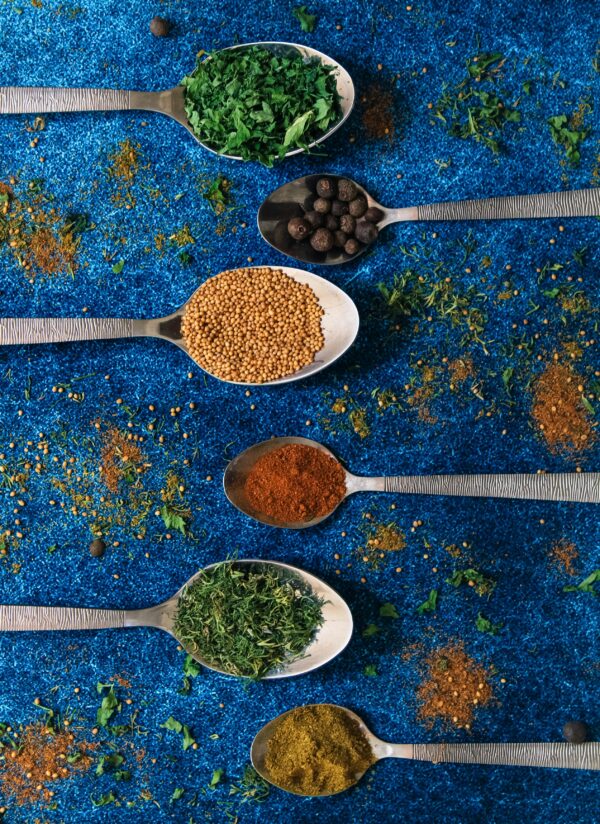 Colorful spices in spoons on a vibrant blue background, showcasing culinary variety.