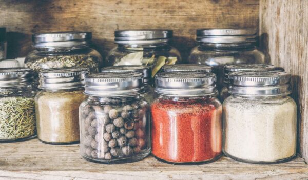 A collection of assorted spices in glass jars on a rustic wooden shelf for culinary use.