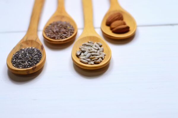 Close-up of various nuts and seeds in wooden spoons on a white background, showcasing healthy food options.