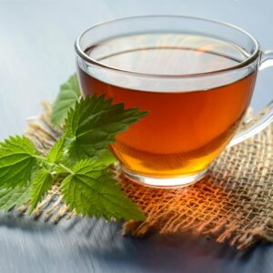 A close-up of herbal tea in a glass cup with fresh mint leaves on a table.