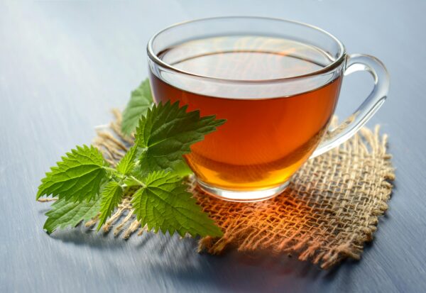 A close-up of herbal tea in a glass cup with fresh mint leaves on a table.